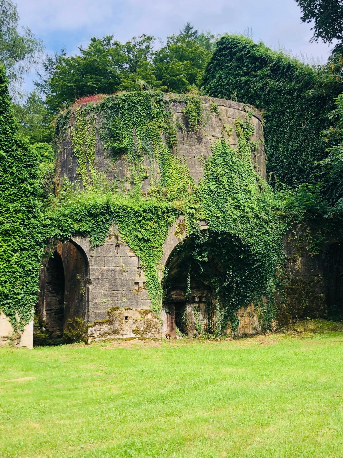 Vestige monumental de l'ancien fourneau, couvert de végétation et vu depuis la pelouse.