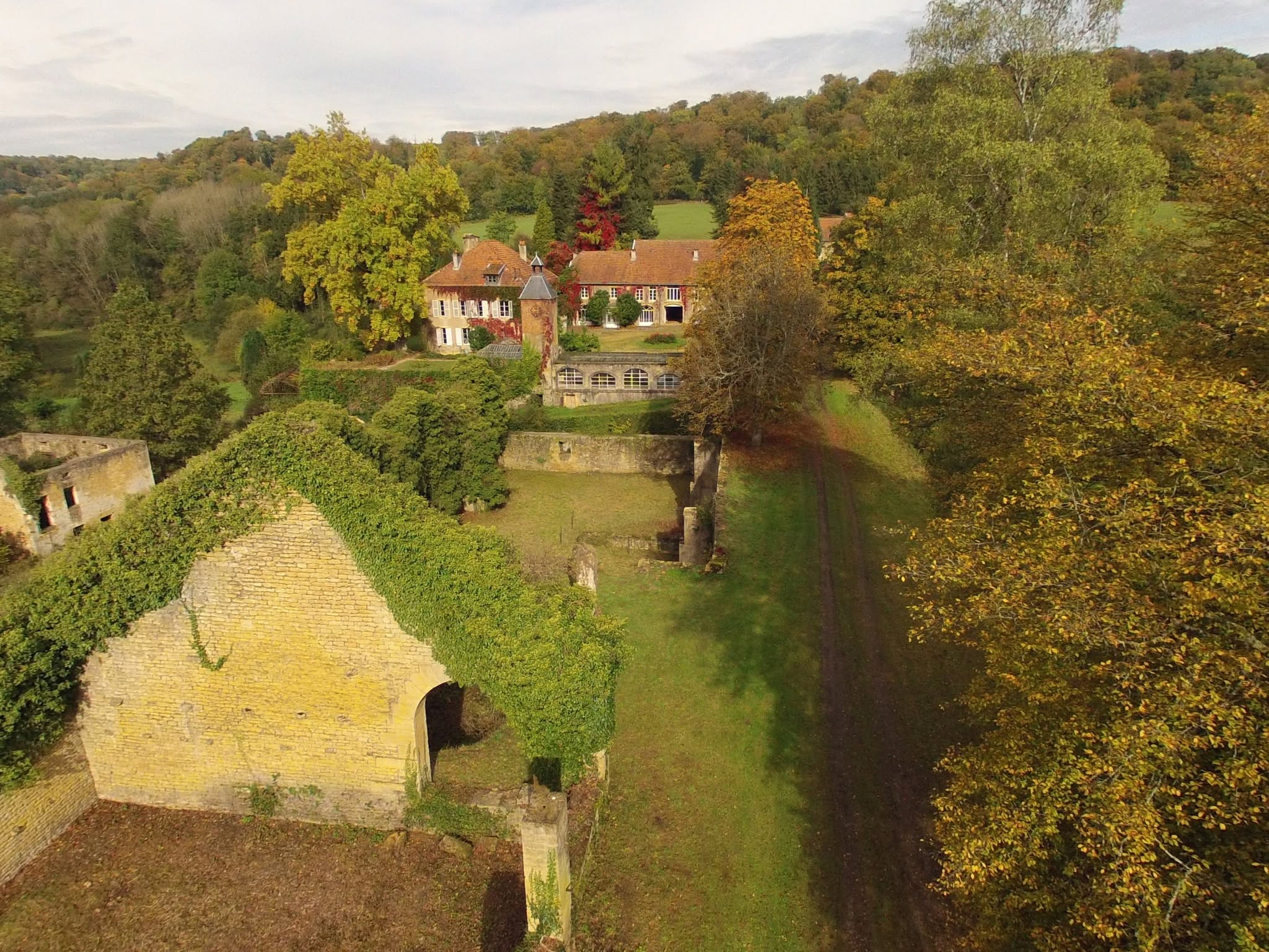 Vue aérienne des Forges de Buré d'Orval montrant les bâtiments, la tour, les vestiges, la prairie et la vallée boisée.