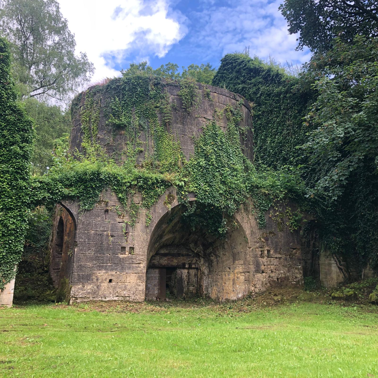 Vue large du vestige monumental de l'ancien fourneau, entouré d'arbres et de végétation.