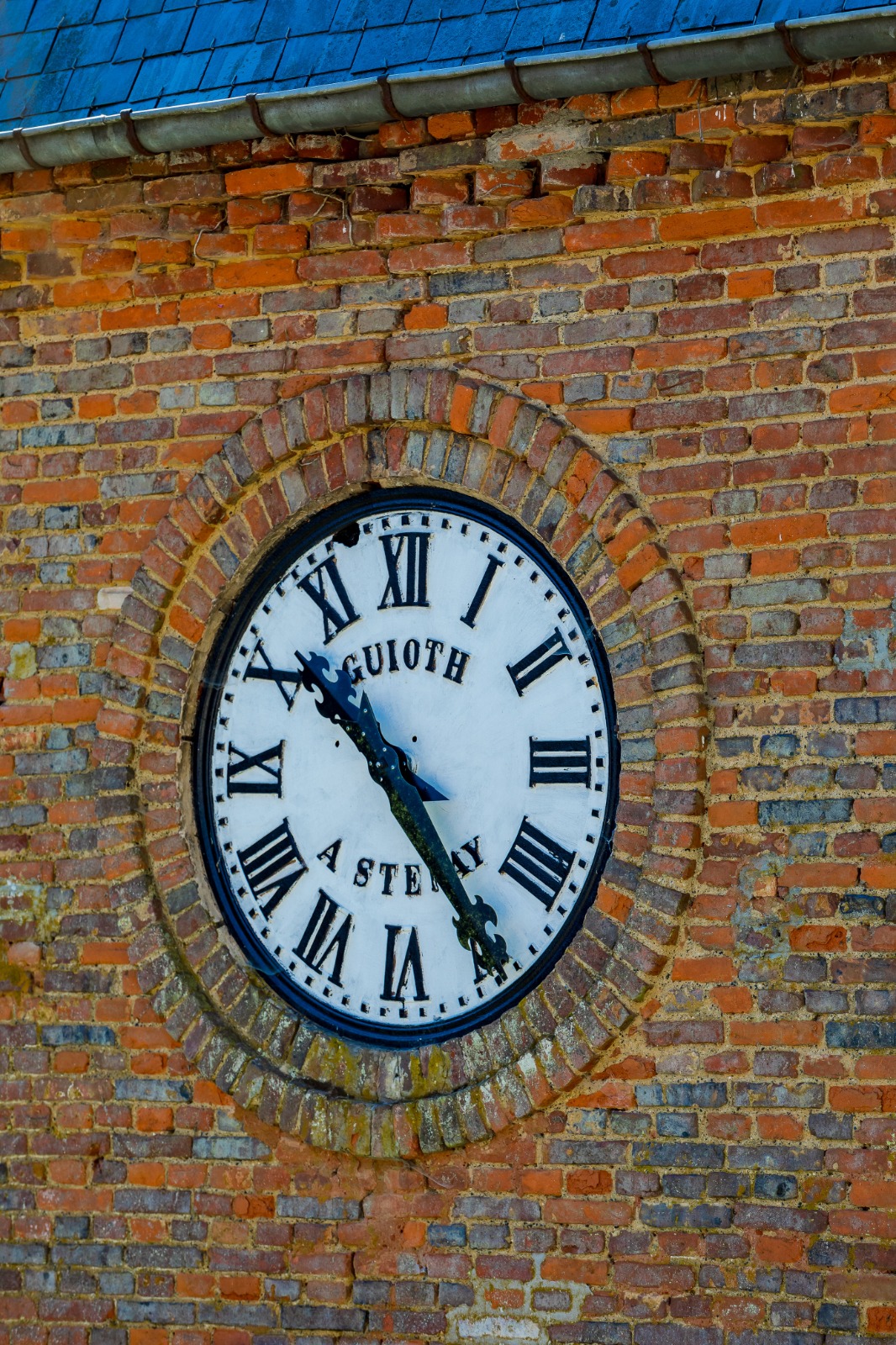 Gros plan du cadran de l'horloge enchâssé dans une maçonnerie de briques.